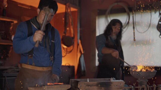 One man use hammer to work as blacksmith to create horseshoe stay and support by senior man with both wear cowboy costume.