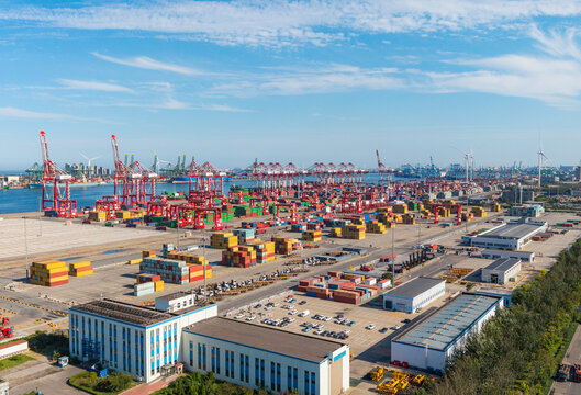 Large port container yard with red gantry cranes and stacked shipping containers under clear blue sky