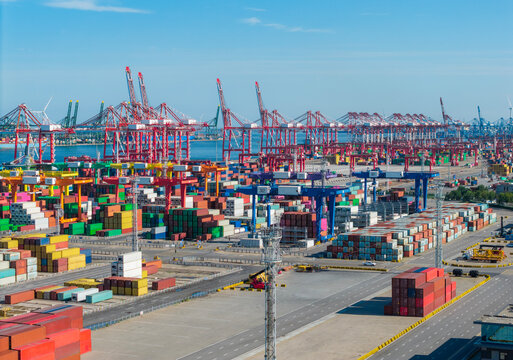 Large port container yard with red cranes and stacked shipping containers under clear blue sky