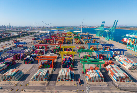Large port container yard with crane operations and colorful shipping containers under clear sky