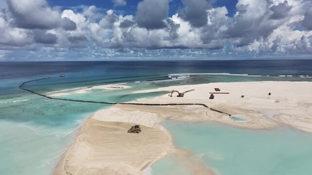 Aerial view of land reclamation and beach construction with excavators on white sand and turquoise lagoons in Gulhi, Kaafu Atoll, Maldives.