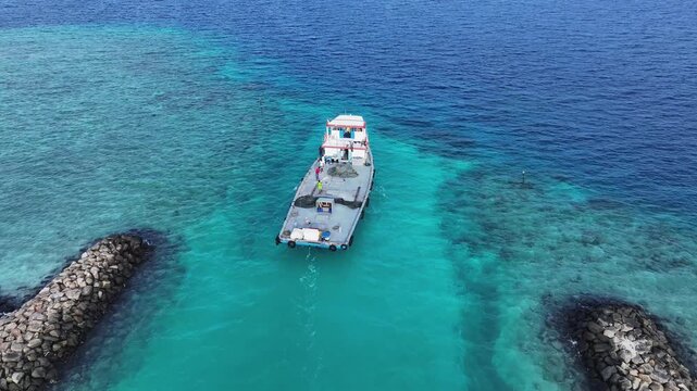 Aerial view of a boat navigating a narrow turquoise channel between stone breakwaters with people on board Gulhi, Kaafu Atoll, Maldives.