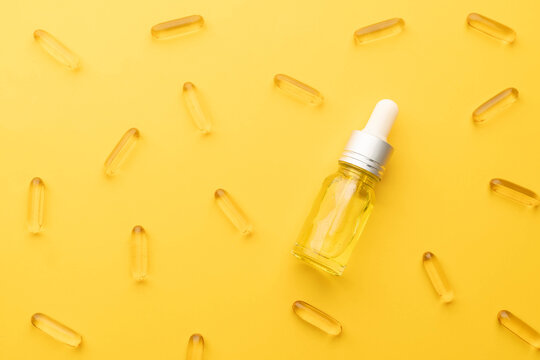 Oil capsules and serum bottle with dropper on yellow background. Nutritional supplement contains fish oil, omega 3, omega 6, omega 9, vitamin e, vitamin d and vitamin. Health care and beauty concept.