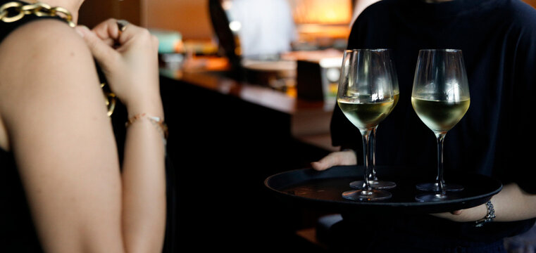 Elegant waiter serving white wine on a tray in a luxury rooftop restaurant, capturing a refined fine dining experience with a sophisticated ambiance and city view. Professional hospitality scene