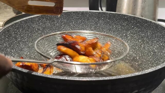 Scooping fried plantain slices from hot oil using mesh strainer