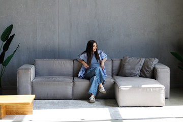 Obraz premium Young lady sitting on sofa, relaxing looking at the camera at home.