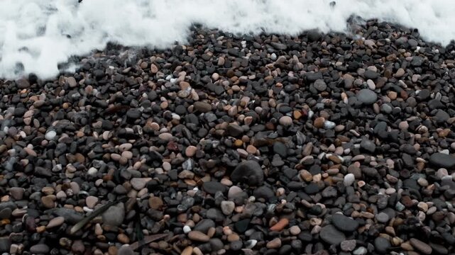Close up of crystal clear sea water washing over wet dark pebbles on the beach during a sunny day