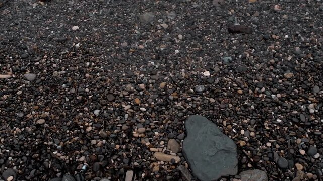 Top down view of white sea foam and water receding on dark grey pebbles of the Mediterranean shore