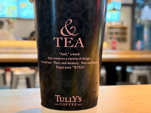 Tully's Coffee andTEA paper cup held upside down with black ornate pattern through a glass window at the Ariake Garden ABC-MART - Tokyo, Japan, December 16, 2025