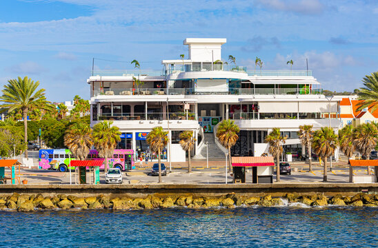 Willemctad, Curacao - 22.03.2026: Modern white waterfront building with restaurants and colorful tour buses parked in front in Willemstad Curacao