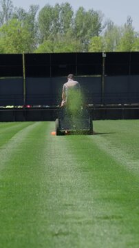 Groundskeeper mowing and maintaining a professional sports field with a riding lawn mower. Freshly cut green grass on stadium turf under bright daylight with striped mowing pattern.