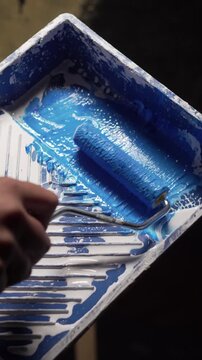 applying blue paint with a roller next from paint tray in studio setting. Close-up.