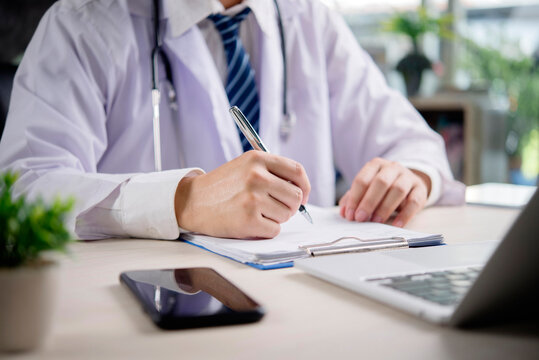 Doctor writing medical record prescription document healthcare clinic stethoscope desk laptop hospital patient health treatment diagnosis professional physician administration concept.