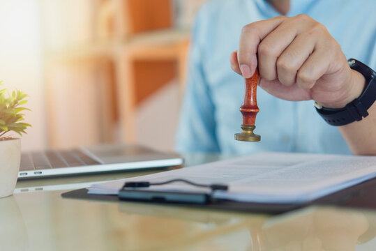 Manager hand stamping approval form document office workspace. Quality control certification business bureaucracy visa approval certified paperwork laptop background.