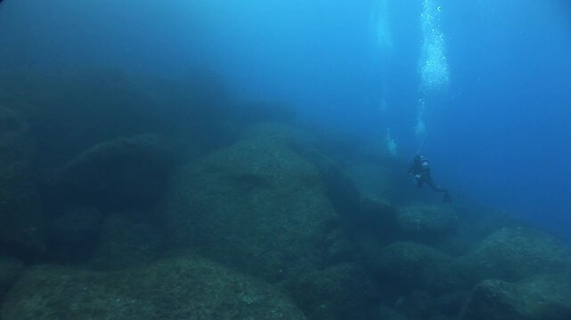  scuba divers exploring   reefs walls and caverns  underwater deep blue water big rocks and bubbles ocean scenery 