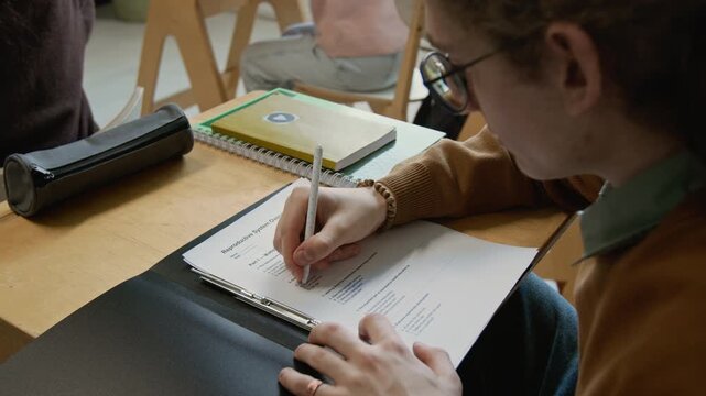 Arc close-up of face of diligent nerdy young Caucasian teenage male student performing multiple choice test at lesson, glancing up at blackboard, choosing correct answer to check comprehension