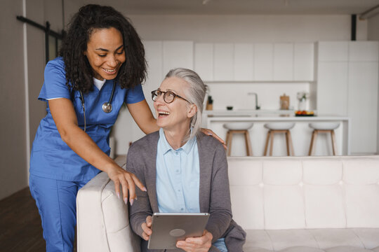 Smiling nurse and happy senior woman using tablet at home, healthcare support, elderly care, medical assistance, digital communication, caregiver help, rehabilitation and modern home care concept