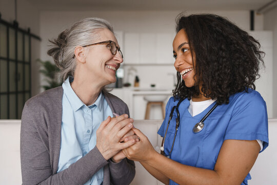 Elderly woman and nurse holding hands at home on couch, healthcare support, caregiving, compassion, trust, medical care, recovery and modern home care concept