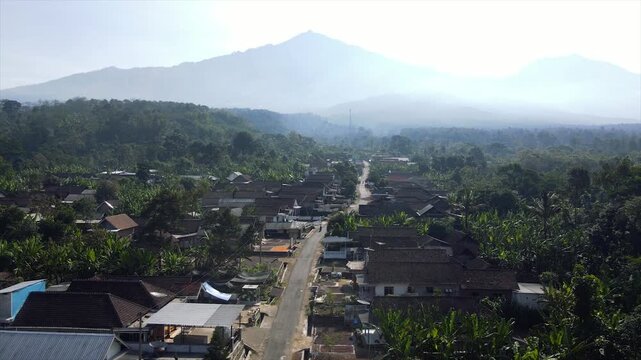 4K aerial drone footage of a peaceful rural village at the foot of the misty peaks of Mount Arjuna.