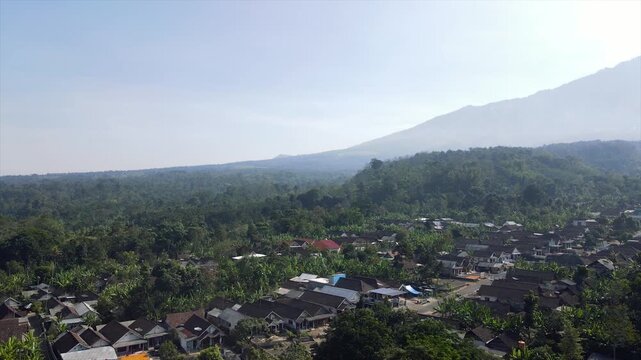 4K aerial drone footage of a peaceful rural village at the foot of the misty peaks of Mount Arjuna.
