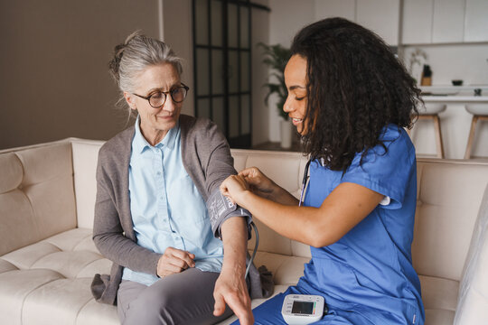 African-American nurse checking blood pressure of elderly woman at home, healthcare worker examining senior patient, medical care, home assistance and rehabilitation concept