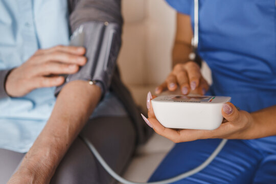 Close up of young nurse measuring blood pressure of senior woman at home, healthcare worker providing medical checkup, health examination, elderly care, home visit and support concept