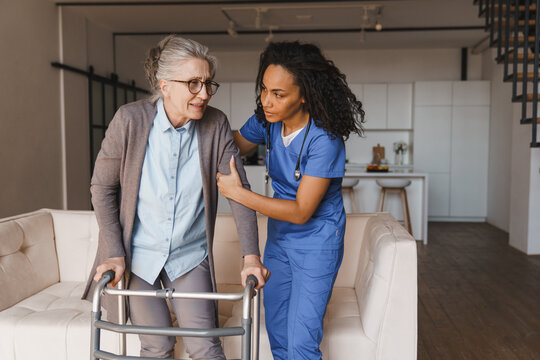 Senior woman walking with walker while nurse helps her at home, caregiver supporting elderly patient with mobility assistance, rehabilitation, home care service and healthcare concept copy space