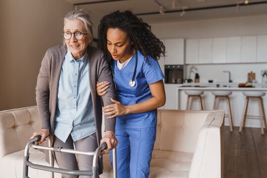 Female nurse helping senior woman walk with walker at home, caregiver assisting elderly patient with mobility support, rehabilitation and home care service concept copy space