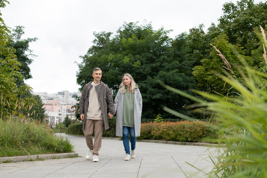 Couple walking together holding hands in green city park