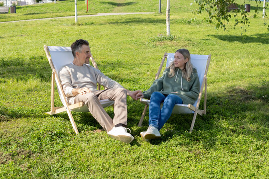 Happy couple holding hands while relaxing on deck chairs in park