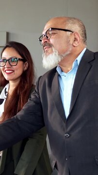 Indian Asian young business professional or businessman confidently shaking hands across a table with a colleague after finalizing a significant business deal or new project in modern corporate office