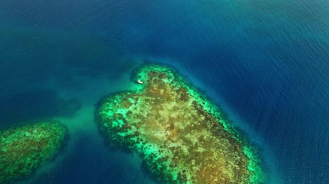 Aerial view of a vibrant coral reef surrounded by deep blue turquoise waters in Guanaja, Bay Islands Department, Honduras.