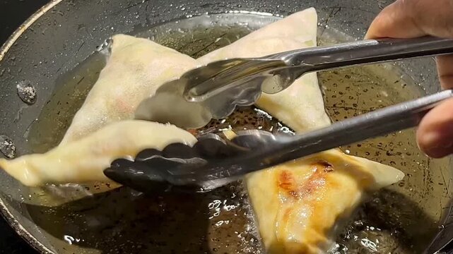 Tongs turning samosas frying in hot cooking oil close up
