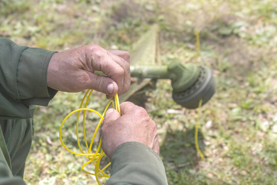 Close-up of worker hands replacing yellow nylon line in grass trimmer head