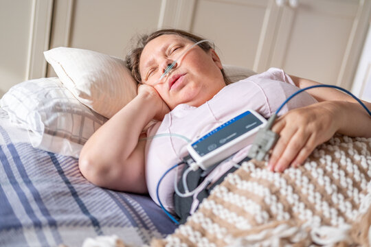 Woman resting in bed with home medical monitoring device, nasal cannula oxygen, apnea monitoring, pulse oximeter home healthcare, COPD quiet recovery, screening and treatment chronic sleep deprivation