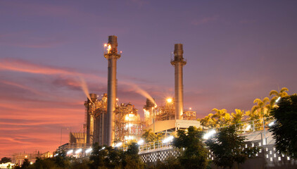 Fototapeta premium Modern power plant with chimney smokestacks and green environment against blue sky.Eco-friendly natural gas power plant surrounded by green trees and tropical garden.