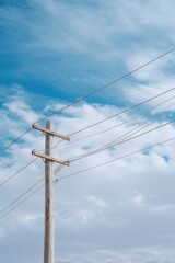Fototapeta premium Wooden electric utility pole power lines against blue cloudy summer