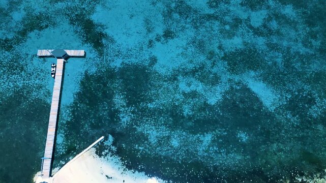 Aerial view of a T-shaped wooden pier extending into crystal clear turquoise waters along a white sand beach in Guanaja, Bay Islands Department, Honduras.