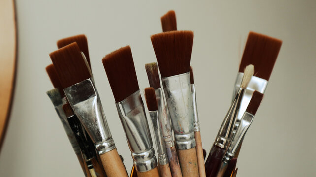 Primo piano artistico di una collezione di pennelli da pittura professionali di diverse dimensioni e forme custoditi in un contenitore all'interno di un atelier d'arte.