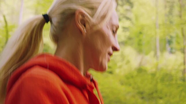 A caucasian woman hikes through a vibrant forest in springtime, wearing a red jacket and enjoying the fresh air. Showing the serene beauty of nature, with green foliage surrounding her.