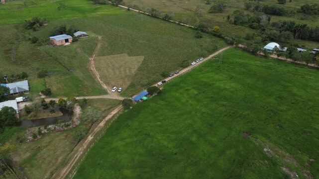Top down aerial view of rural dirt road with vehicles, farm pond and rice fields in Casanare, Colombia