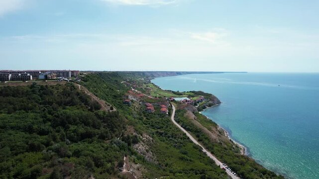 Aerial view of the rugged Black Sea coastline with steep cliffs, lush green hills, and coastal resorts under a clear blue sky in Balchik, Dobrich Province, Bulgaria.