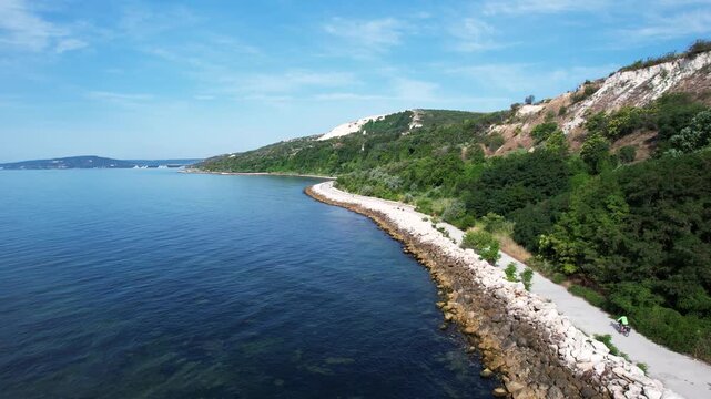 Aerial view of the Black Sea coastline with white cliffs, lush green hills and a stone promenade along the shore in Balchik, Dobrich Province, Bulgaria.