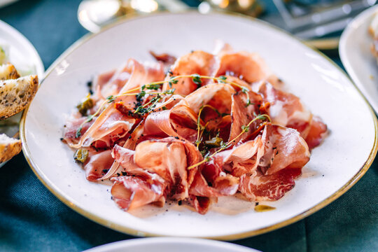 Prosciutto and cured meats on a white plate garnished with herbs and capers for appetizer