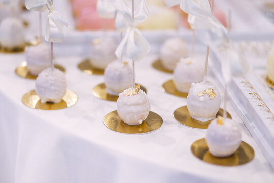 Elegant white cake pops with gold leaf and ribbons for wedding dessert table and celebration
