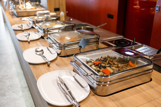 Self-serve hot buffet with stainless steel chafing dishes and plates at a modern restaurant