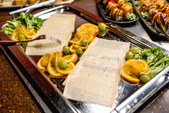 Sliced cheese platter with orange slices and grapes on a buffet tray for catered event
