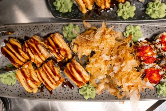 Overhead view of sushi rolls with wasabi, bonito flakes and sauces on a speckled plate at a restaurant