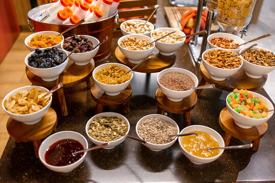 Breakfast buffet display with bowls of nuts, seeds, dried fruit, cereal toppings and condiments