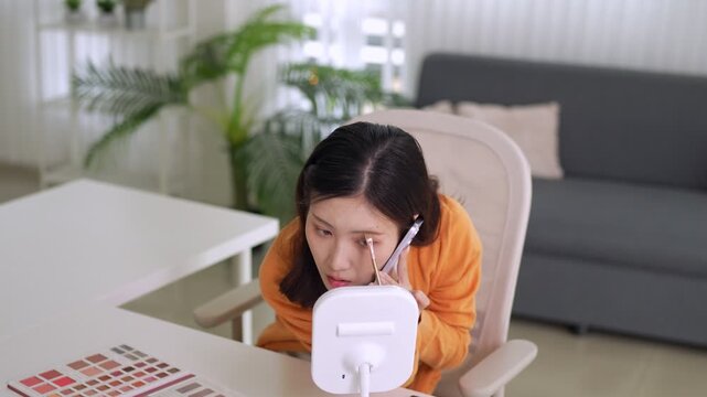 young Asian women makeup artist talking phone call working color palette cosmetics beauty product review influencer content creator skincare tutorial home